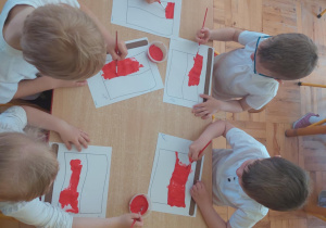 dzieci malują czerwoną farbą połowę narysowanej flagi