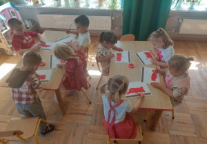 dzieci malują czerwoną farbą połowę narysowanej flagi