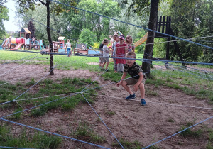 dzieci przechodzą przez labirynt sznurków zawieszonych na różnych poziomach , między drzewami w ogrodzie przedszkolnym