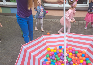 przedszkolaki wrzucają kolorowe piłeczki do odwróconego, dużego parasola