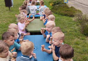 dzieci jedzą lody siedząc w ogrodzie