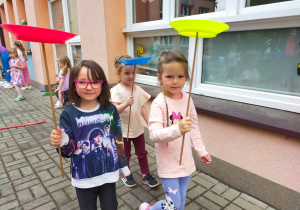 dziewczynki idą trzymając patyki z umieszczonymi na nich kolorowymi talerzami