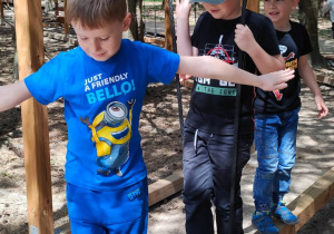 chłopcy idą po zawieszonej kłodzie
