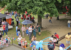 widok z okna na piknikujących ludzi w ogrodzie przedszkolnym podczas festynu