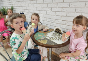 dzieci siedzą przy stolikach w cukierni i jedzą lody