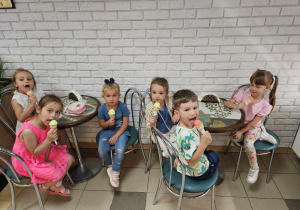 dzieci siedzą przy stolikach w cukierni i jedzą lody