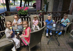 dzieci siedzą przy stolikach na dworze i jedzą lody
