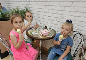 dzieci siedzą przy stolikach w cukierni i jedzą lody