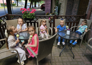 dzieci siedzą przy stolikach na dworze i jedzą lody