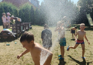 chłopcy przebiegają pod prysznicem wody w ogrodzie przedszkolnym