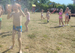 dzieci biegają pod kroplami deszczu w ogrodzie przedszkolnym