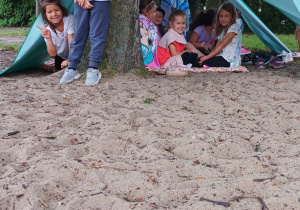 dzieci pod namiotami wykonanymi z materiału zawieszonego na sznurku rozciągniętym pomiędzy drzewami