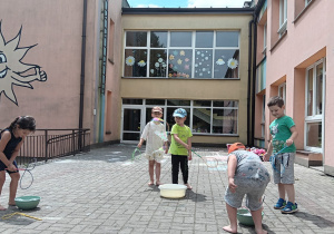 dzieci puszczają duże bańki mydlane na tarasie przedszkolnym