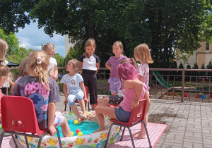 dziewczynki siedzą na krzesełkach wokół basenu z wodą i piłeczkami i probują je złapać i wyciągnąć stopami
