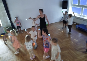 dzieci z nauczycielką bawią się światłem z latarek w zaciemnionej sali