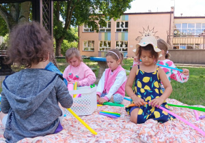 dzieci w ogrodzie bawią się rurkami antystresowymi siedząc na macie na trawie