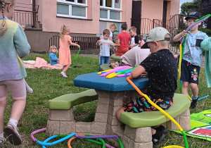 dzieci w ogrodzie bawią się rurkami antystresowymi siedząc na macie na trawie