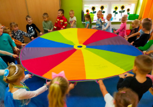 przedszkolaki w sali w czasie zabaw z chustą animacyjną krążą w kole