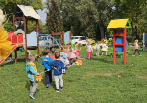 przedszkolaki idą w korowodzie po ogrodzie przedszkolnym