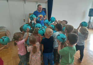 dzieci stoją z piłkami uniesionymi w górę przy trenerze