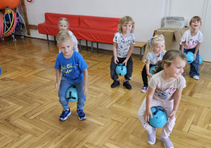 przedszkolaki skaczą z piłkami umieszczonymi między kolanami