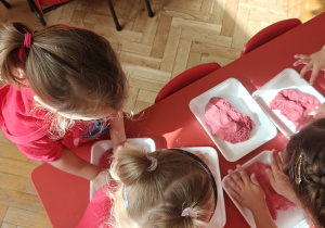 dzieci ubrane na czerwono ugniatają czerwoną masę