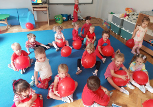 przedszkolaki siedzą z czerwonymi balonami na macie