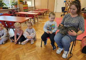 mama siedzi na krzesełku i na kolanach trzyma kota i pokazuje go dzieciom