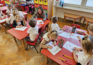 dzieci siedzą przy stolikach i wykonują pracę