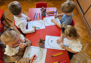 dzieci siedzą przy stolikach i wykonują pracę