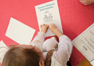 dziewczynka nakleja naklejkę na paszporcie odkrywcy Praw Dziecka