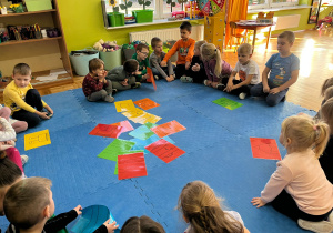 dzieci siedzą w kole i przyglądają się rozrzuconym puzzlom z kredkami