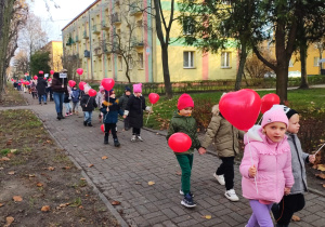 dzieci idą ulicami osiedla z czerwonymi balonami w kształciie serc