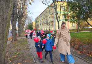 dzieci idą ulicami osiedla z czerwonymi balonami w kształciie serc