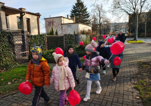 dzieci idą ulicami osiedla z czerwonymi balonami w kształciie serc