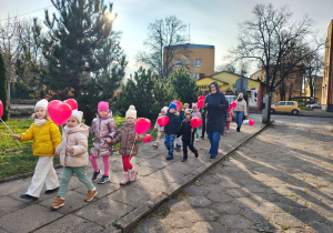 dzieci idą ulicami osiedla z czerwonymi balonami w kształciie serc