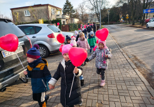 dzieci idą ulicami osiedla z czerwonymi balonami w kształciie serc