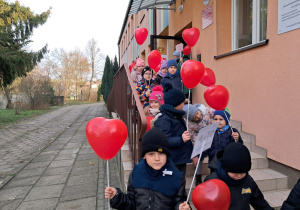 przedszkolaki wychodzą z budynku przedszkola z balonami