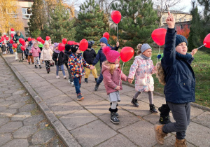 przedszkolaki idą chodnikiem przed przedszkolem z balonami
