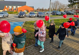 dzieci idą ulicami osiedla z czerwonymi balonami w kształciie serc