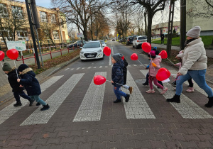 dzieci przechodzą przez ulicę po pasach z czerwonymi balonami w kształciie serc