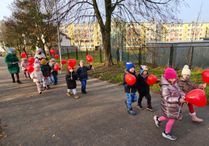 dzieci idą ulicami osiedla z czerwonymi balonami w kształciie serc
