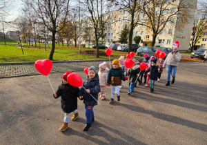 dzieci idą ulicami osiedla z czerwonymi balonami w kształciie serc