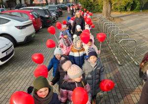 dzieci idą ulicami osiedla z czerwonymi balonami w kształciie serc