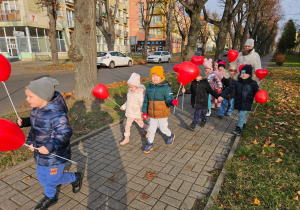 dzieci idą ulicami osiedla z czerwonymi balonami w kształciie serc