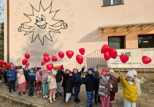 przedszkolaki z balonami czerwonymi w kształcie serc pod budynkiem przedszkola
