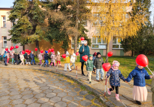 przedszkolaki idą chodnikiem przed przedszkolem z balonami
