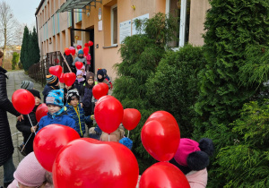 przedszkolaki wychodzą z budynku przedszkola z balonami