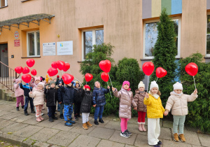 przedszkolaki stoją przed budynkiem przedszkola z balonami