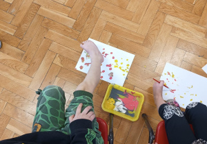przedszkolaki próbują malować pędzelkiem trzymanym przez palce nogi